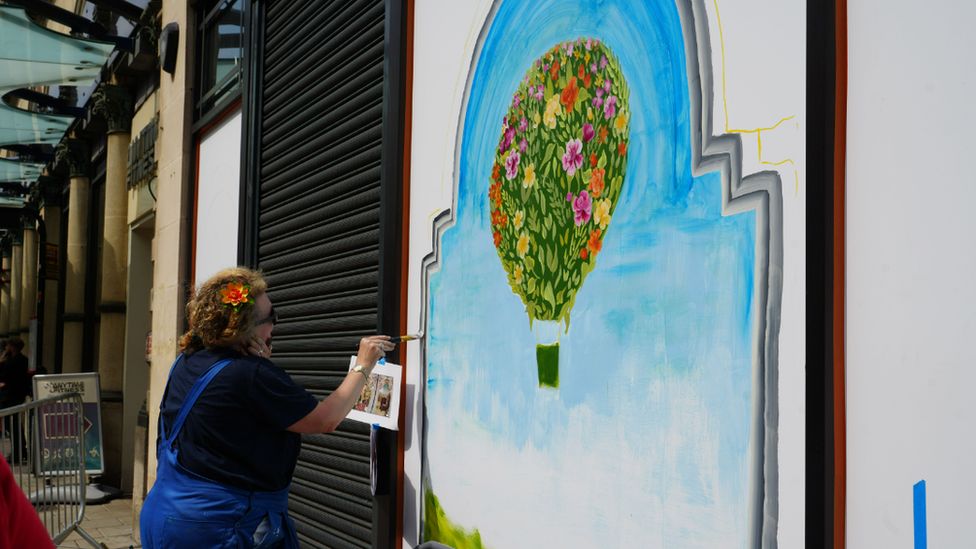 A woman painting a hot air balloon made of flowers onto a wall
