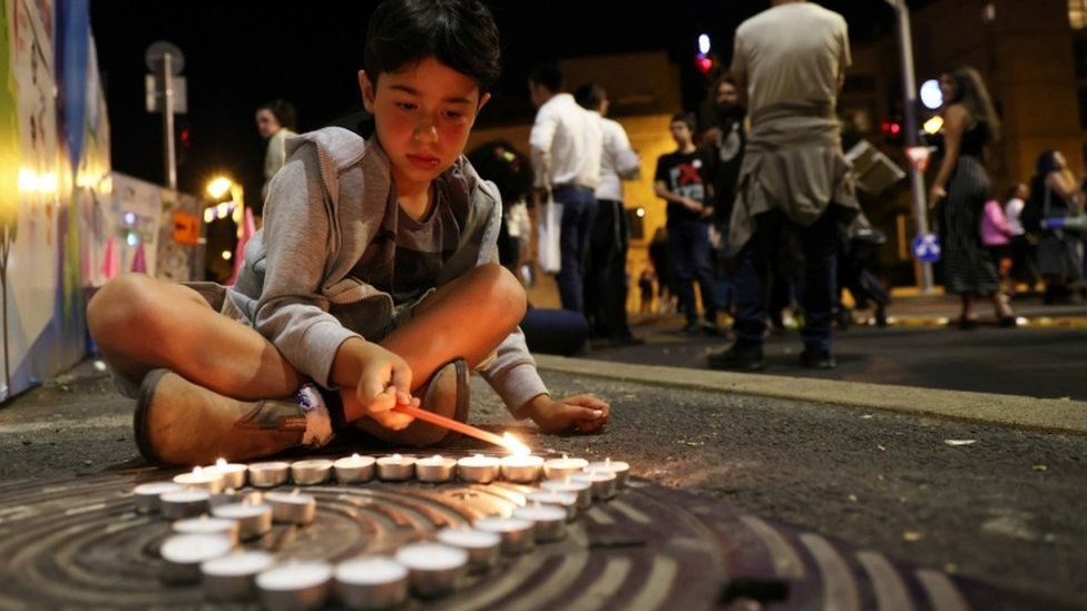 A boy lights candles in a heart shape during a vigil for the people killed and injured in the stampede