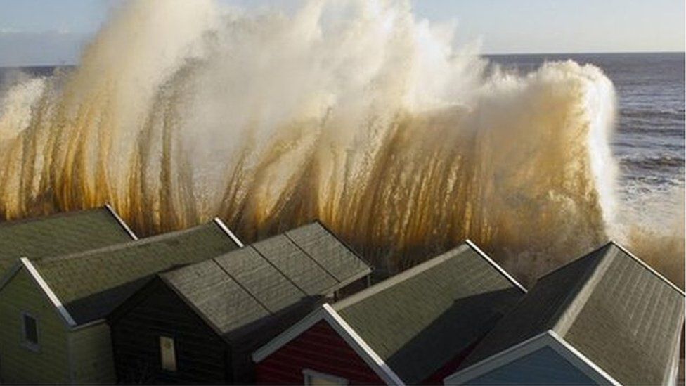Large wave crashing to the shore in front of houses