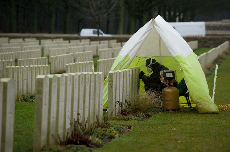 Person covered by a small tent repairing a headstone at Delville Wood Cemetery in France