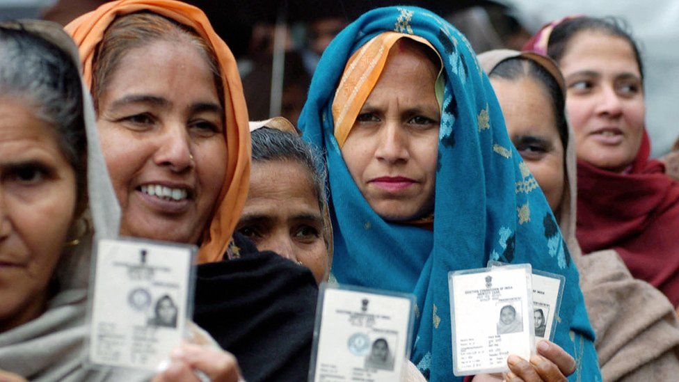 ndian village women hold up their voting cards as they await their turn to vote at a polling station in Majitha