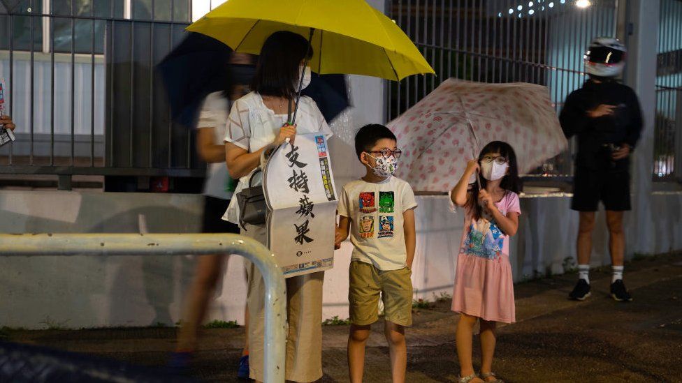A woman holds a copy of the Apple Daily newspaper in front of the Apple Daily headquarters with her children