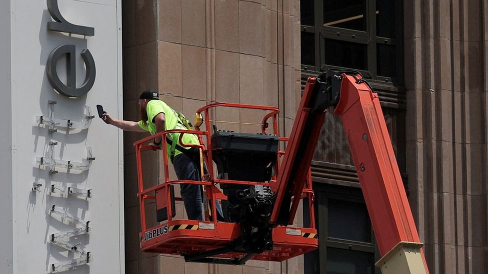 A worker uses a smartphone while dismantling a Twitter's sign at Twitter's corporate headquarters building as Elon Musk renamed Twitter as X and unveiled a new logo, in downtown San Francisco
