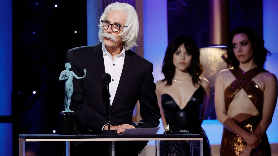 Sam Elliott accepts the Outstanding Performance by a Male Actor in a Television Movie or Limited Series award for 1883 from Jenna Ortega and Aubrey Plaza onstage during the 29th Annual Screen Actors Guild Awards at Fairmont Century Plaza on February 26, 2023 in Los Angeles, California