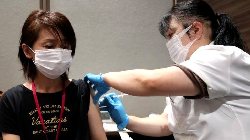 A staff of Japan"s supermarket group Aeon receives a dose of the Moderna vaccine