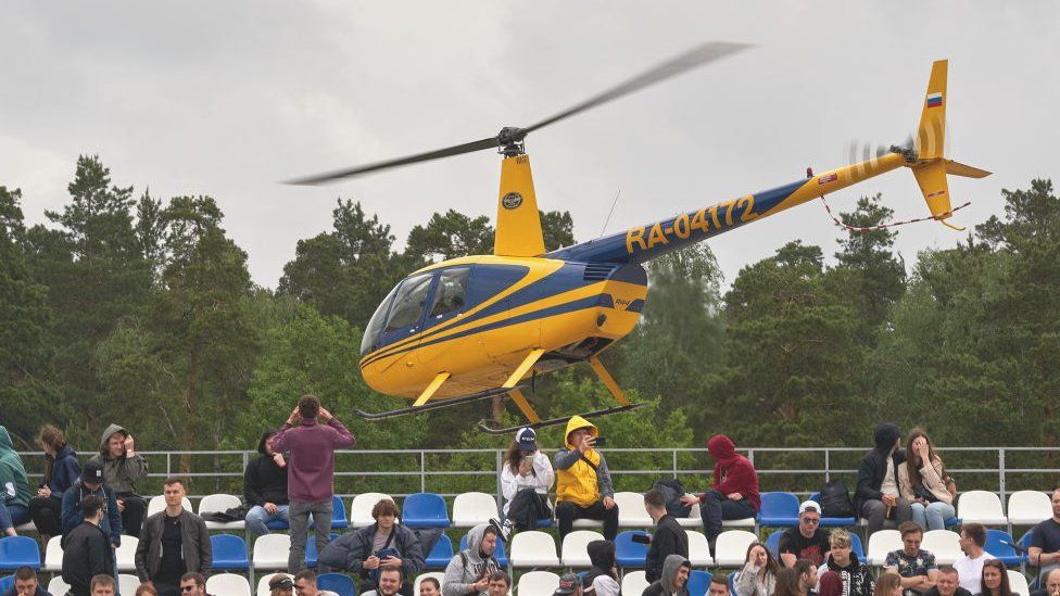 Visitors ride in a yellow Robinson helicopter during a motorsport festival in Russia.