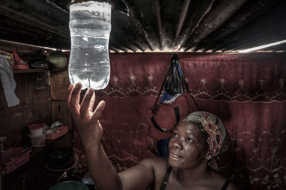 A resident looks at the light beaming from a freshly installed solar light bottle inside her home in the township of Olievenhoutbosch, Centurion, in South Africa. 6 February 2023.