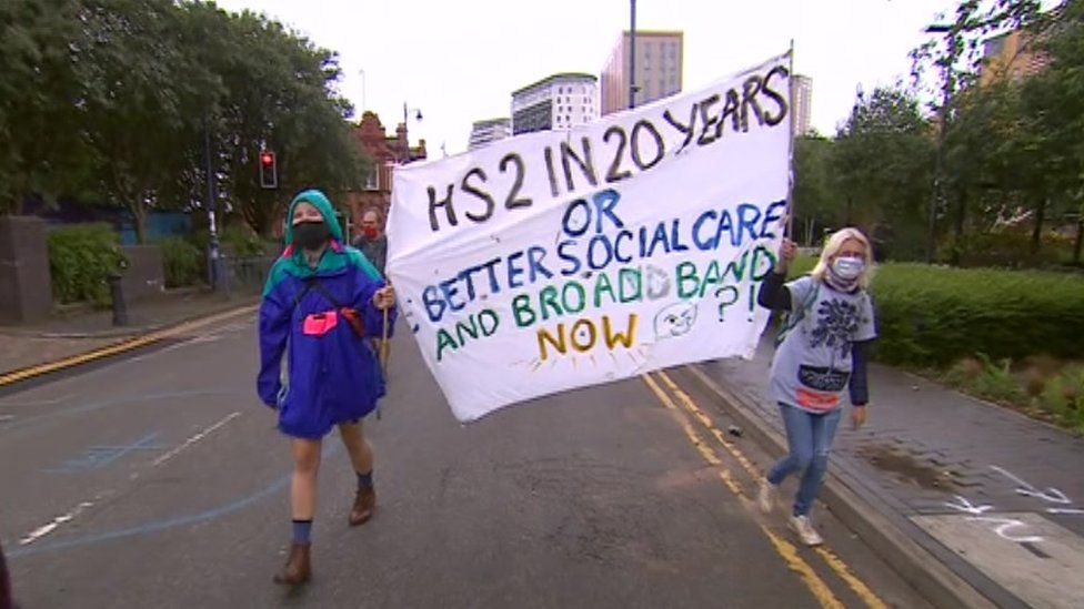 Protesters carry a sign reading "HS2 in 20 years or better social care an broadband now?"