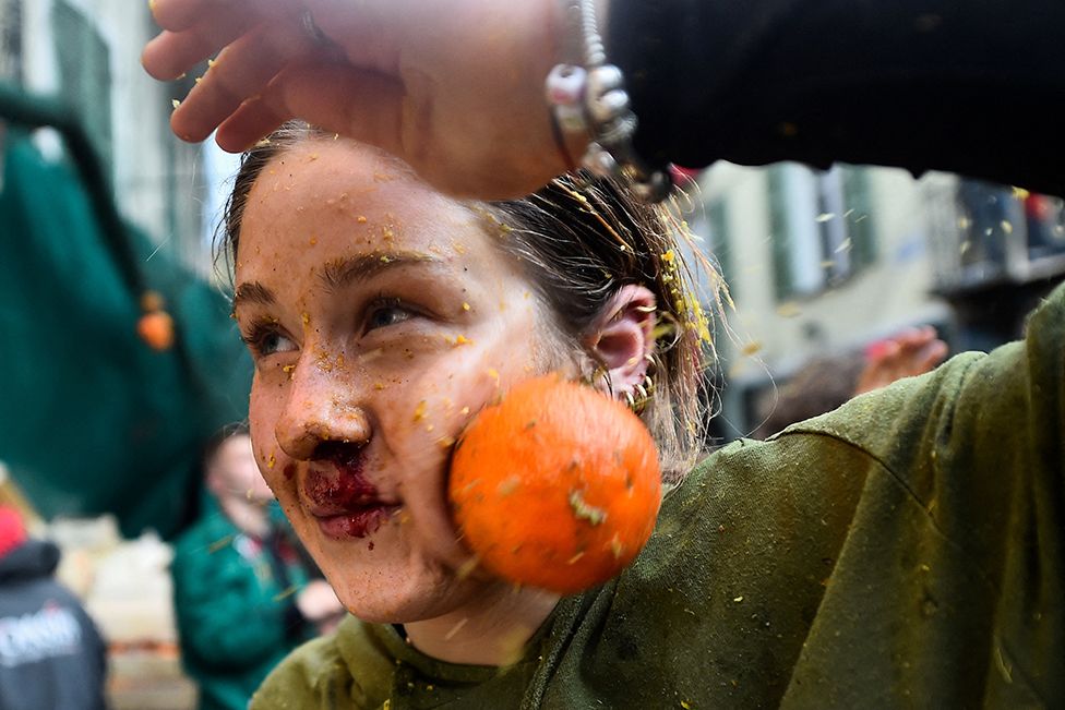 A reveller is hit by an orange as she participates in the annual 'Battle of the Oranges' in the northern city of Ivrea, Italy, on 19 February 2023