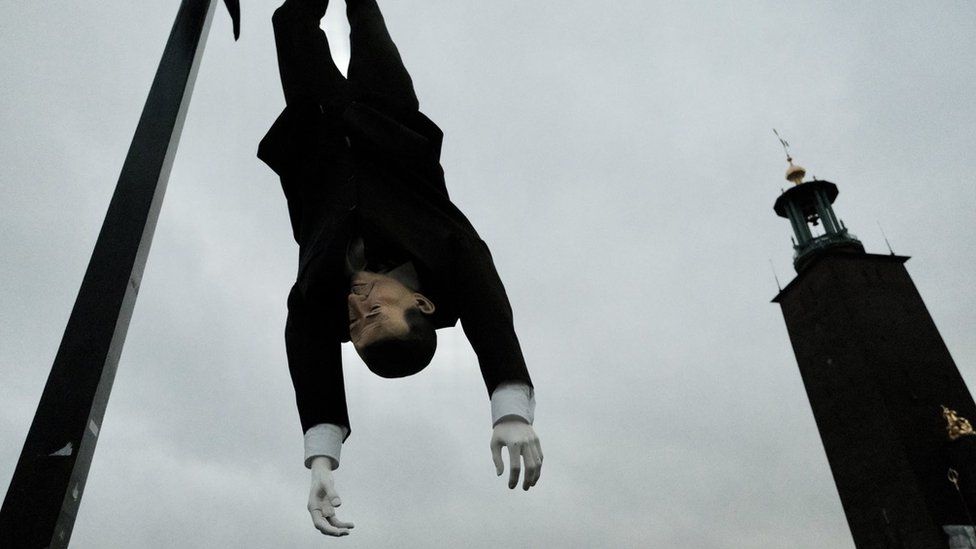 A puppet hanging upside down with Stockholm City Hall visible in the background