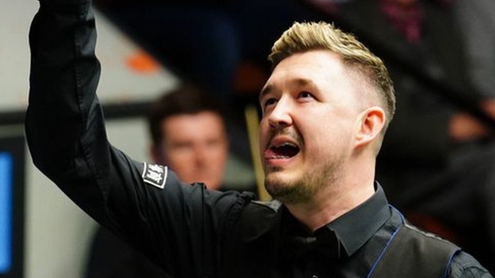 Kyren Wilson wearing black shirt with his arm in the air in front of an audience.