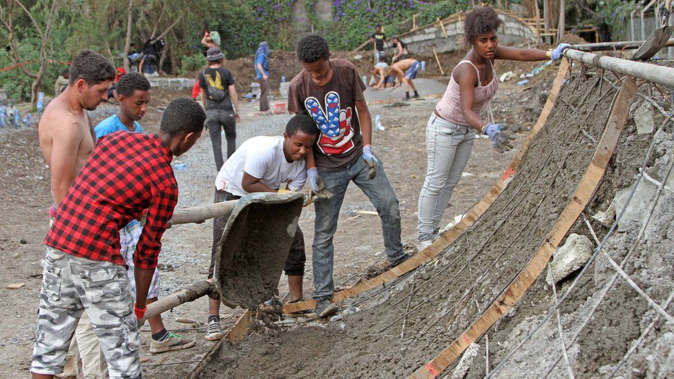 Ethiopian boy pours concrete to make a ramp while four others look on