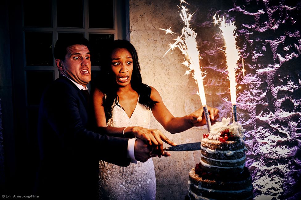 A man and woman cutting a wedding cake that has sparklers on top