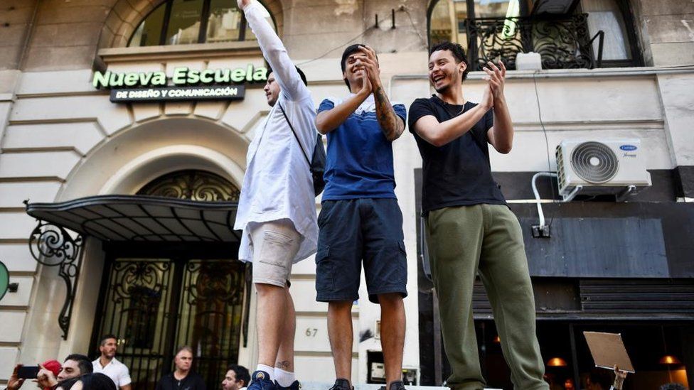 Three men protests stand on a platform clapping during a protest against university cuts in Buenos Aires