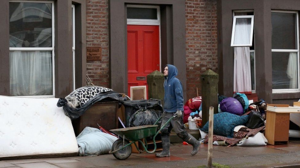 Man with a wheelbarrow in a street where residents have emptied their houses of furniture