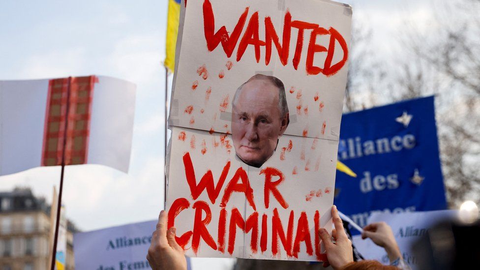A protester in Paris holds a sign accusing Vladimir Putin of war crimes
