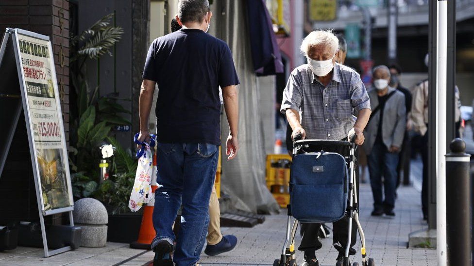 An elderly person walks with the help of his medical chair on the streets of Tokyo