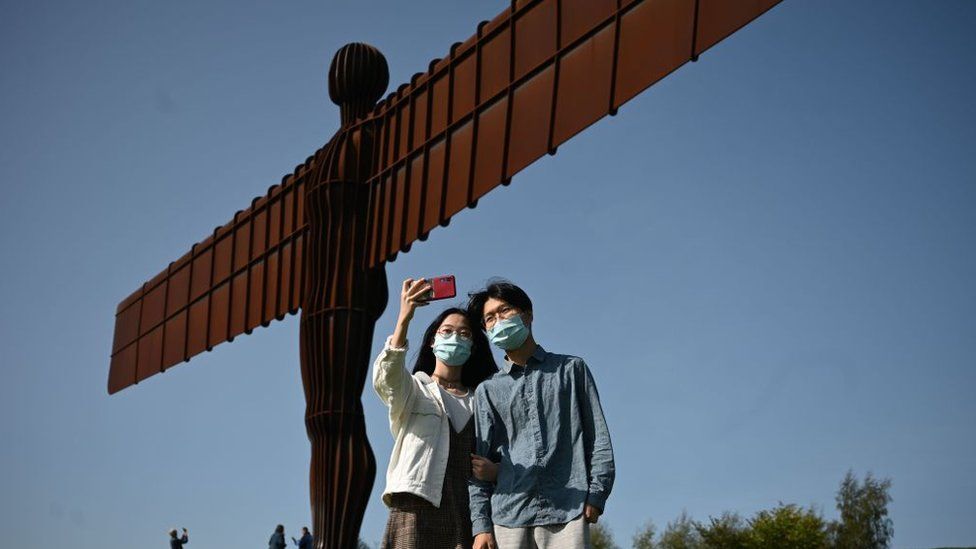 People taking selfies in masks at the Angel of the North