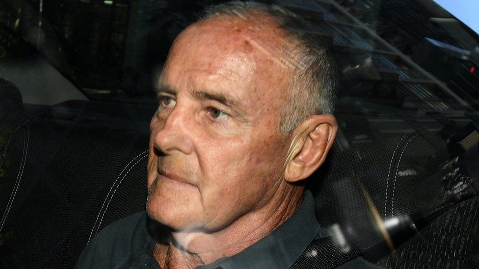Chris Dawson arrives at Sydney police station in a police car