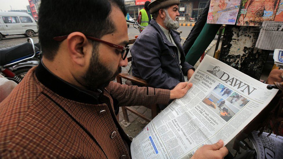 A man reads Dawn newspaper at a news stand