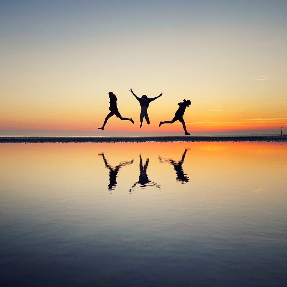 Three children jumping on West Wittering beach in West Sussex