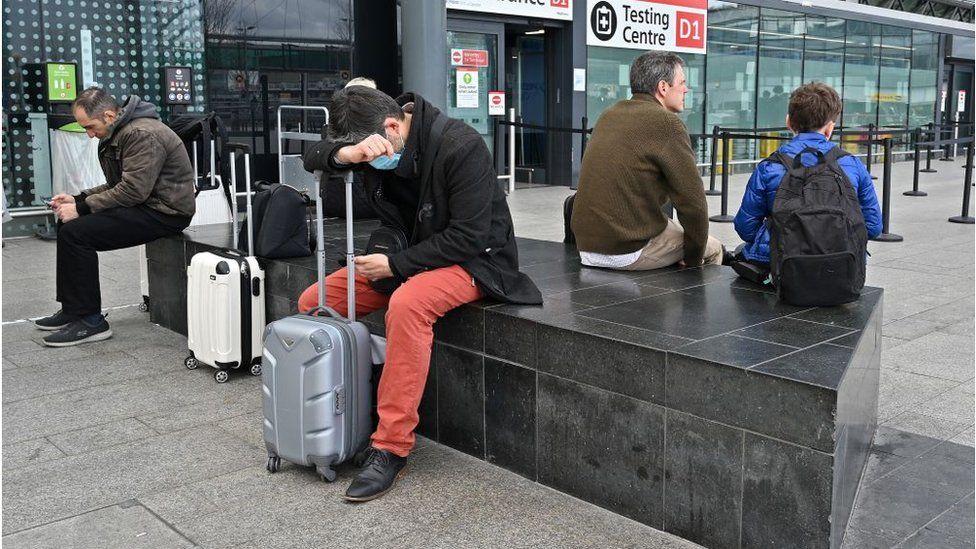นักท่องเที่ยวและผู้เดินทางนั่งนอกศูนย์ทดสอบ Covid-19 ที่อาคาร 3 ของสนามบินลอนดอนฮีทโธรว์ทางตะวันตกของลอนดอน
