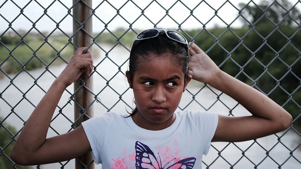 A girl waits on a bridge at the US-Mexico border
