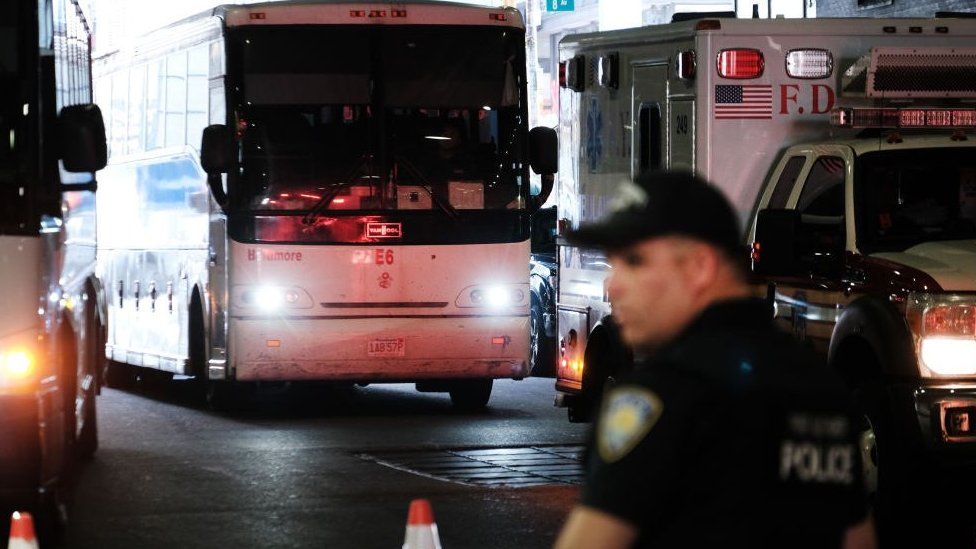 A police man stands in front of a bus carrying migrants that is arriving in New York City from Texas.