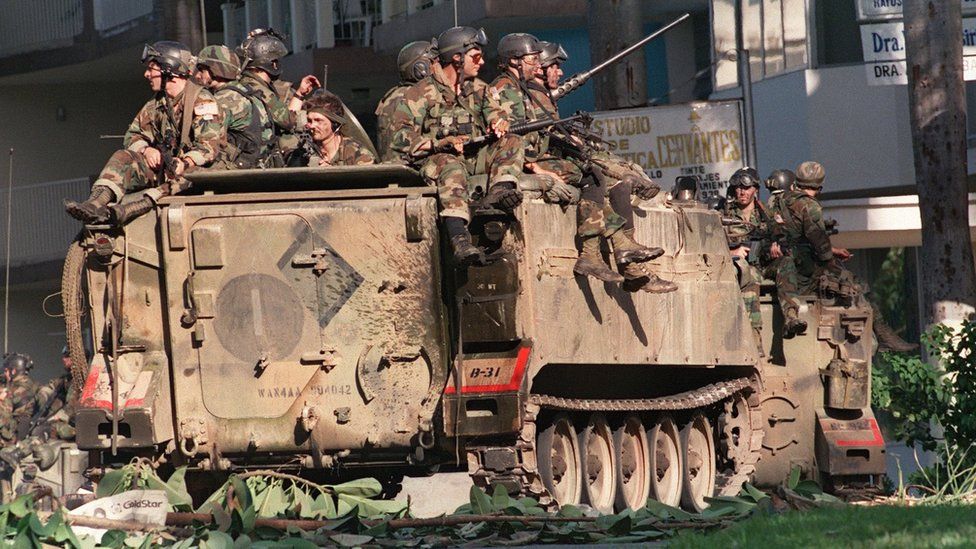 US soldiers sit on top of armoured vehicles in a street of Panama City during Operation Just Cause on 23 December, 1989