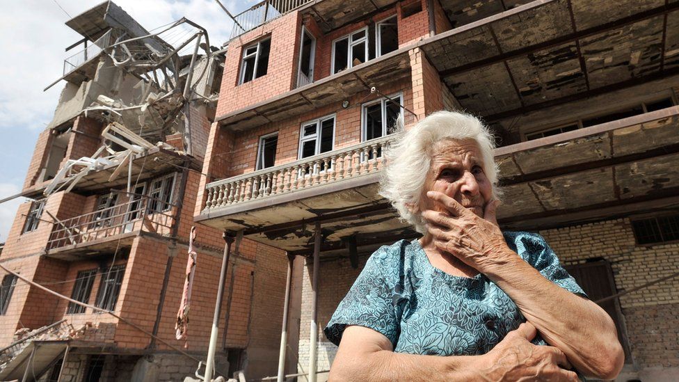 a Georgian woman in front of her home, which has been destroyed