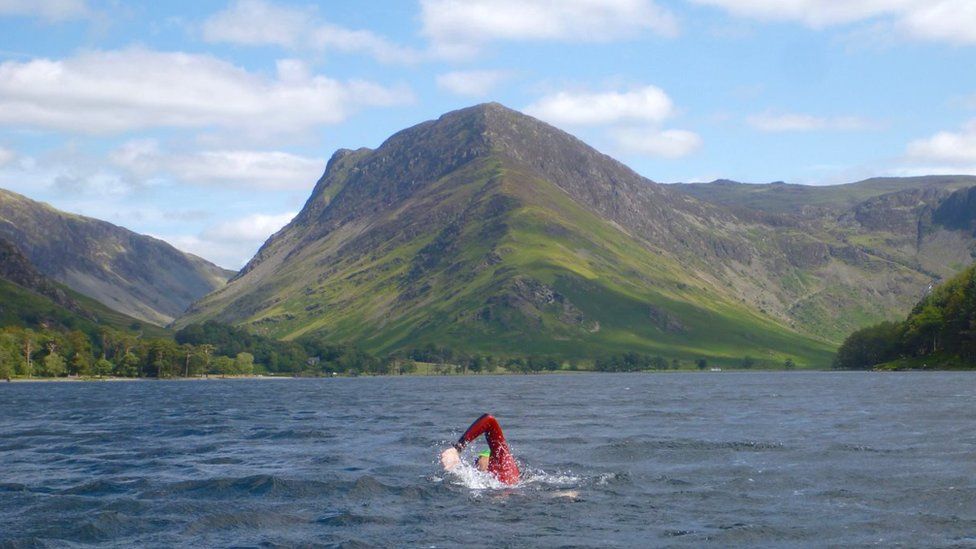 George Taplin swims in front of large hill