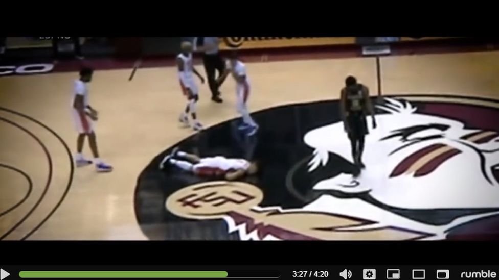 screenshot from video of basketball player face-down on floor with team mates surrounding him