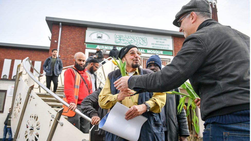 A man hands out flowers to Muslims as they leave Birmingham Central Mosque as Friday prayers finish