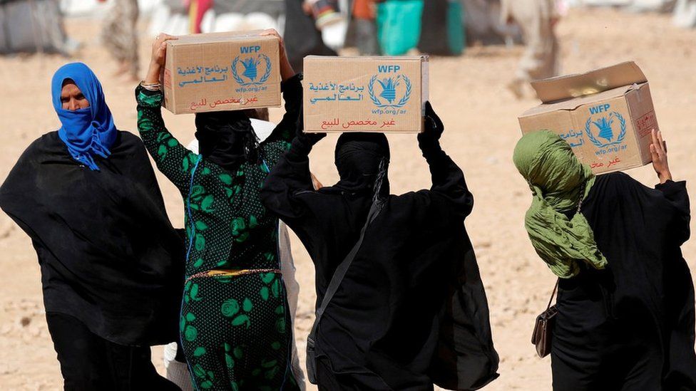 People carry boxes of food aid given by UN's World Food Programme at a refugee camp in Ain Issa, Syria