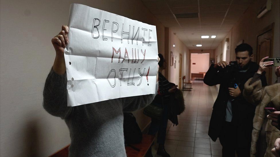 An activist raises a sign at the local court that reads: "Return Masha to her father!"