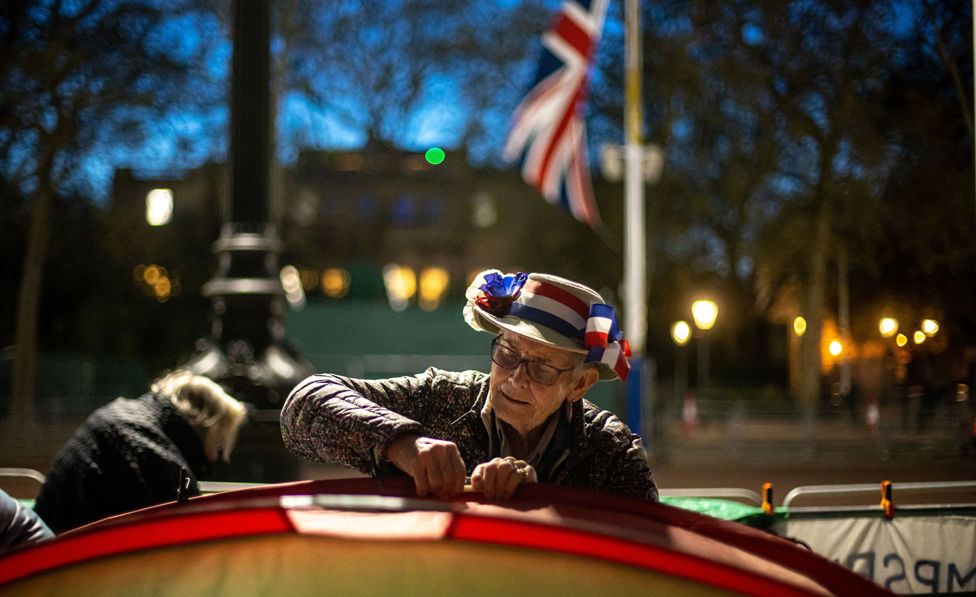 A royal fan prepares his tent as he waits on the coronation procession route on The Mall in London