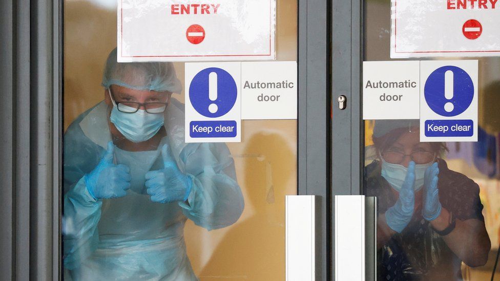 Medical staff in PPE clap through a glass door