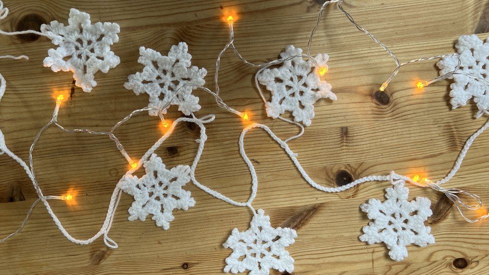 a crocheted snowflake garland on a wooden table alongside fairy lights