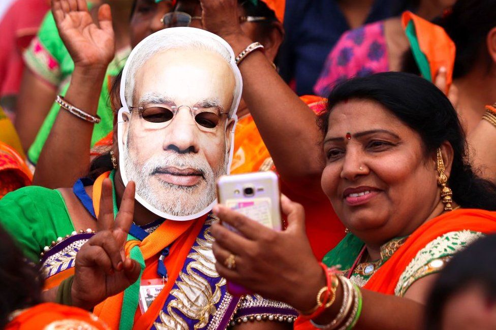 Indian supporters of the Bhartiya Janta Party (BJP), with one wearing a mask of Prime Minister Narendra Modi, take a selfie