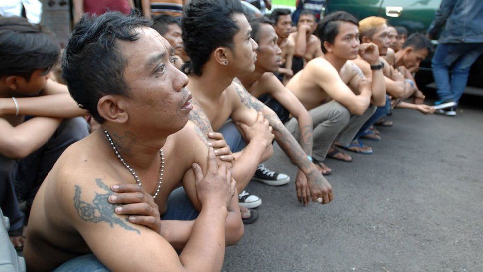 Men accused of being thugs are detained, crouching in a line on the street