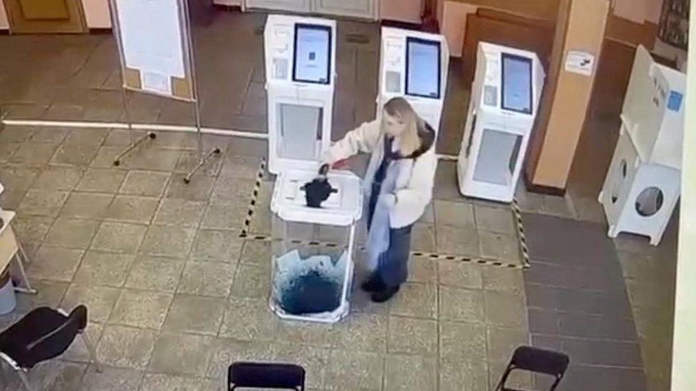 A woman pours a liquid into a ballot box, during the Russian presidential election in Moscow, Russia, in this screen grab taken from a video recording of a screen showing CCTV footage, March 15, 2024