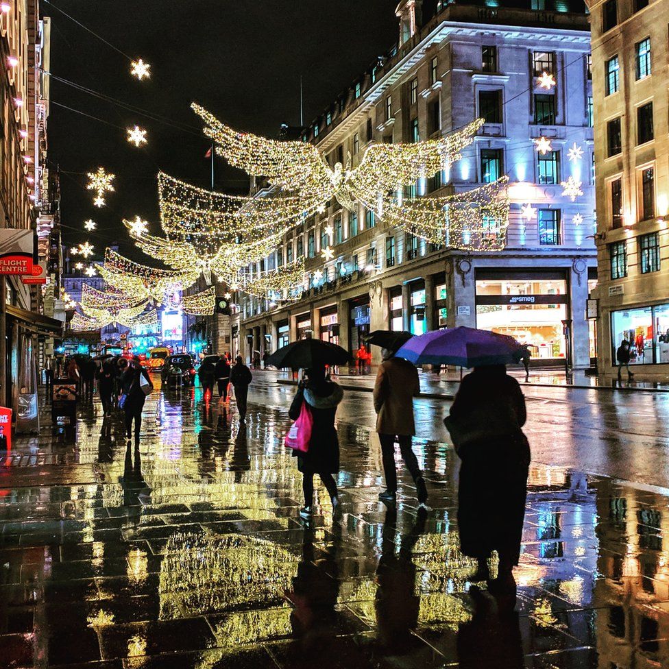 Shoppers and Christmas lights reflected on a wet pavement