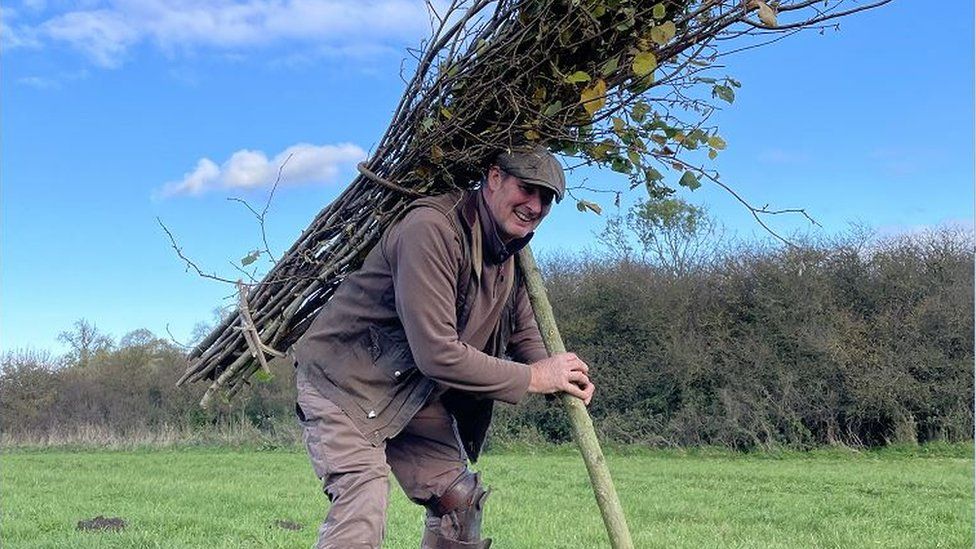 Master thatcher Ellis Butcher recreating the Led Zeppelin photo, stood in a field with sticks on this back