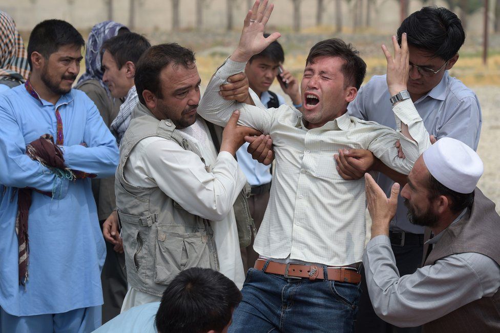 A relative (C) is comforted as he weeps alongside unseen shoes and other belongings of those who were killed in the twin suicide attack, at a mosque in Kabul, 24 July