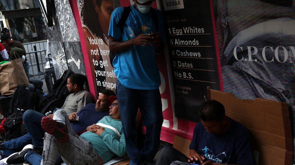 Recently arrived migrants to New York City wait on the sidewalk outside of temporary reception centre