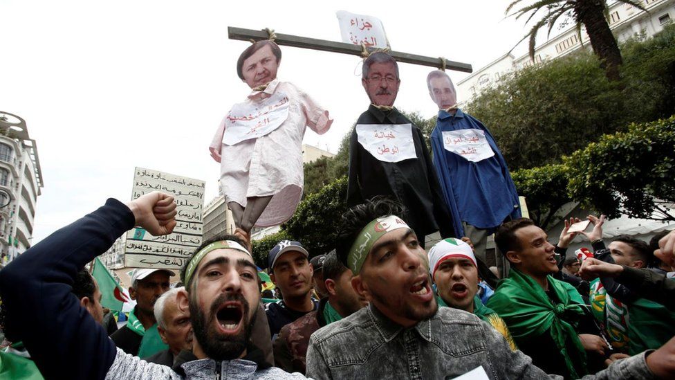 People gesture and carry a mock hangman with the faces of Algerian businessman Ali Haddad, former prime minister Ahmed Ouyahia, and Said Bouteflika, brother of former Algerian president Abdelaziz Bouteflika, during a protest to push for the removal of the current political structure, in Algiers, Algeria April 5, 2019.