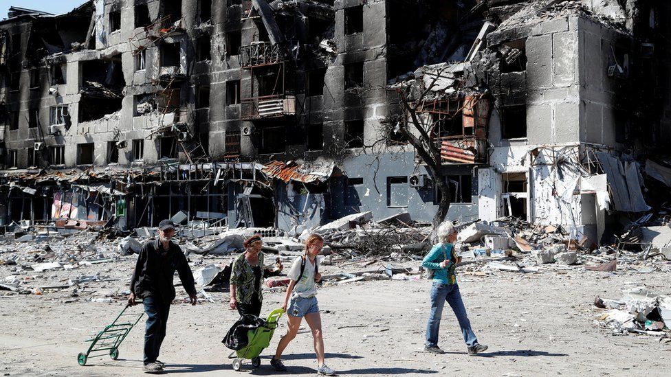 Local residents walk past an apartment building destroyed during Ukraine-Russia conflict in the southern port city of Mariupol