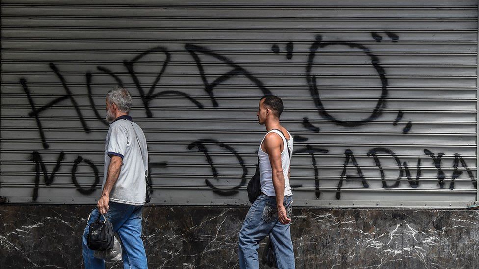 People in Venezuela walk past a graffiti that reads in Spanish "Zero hour"