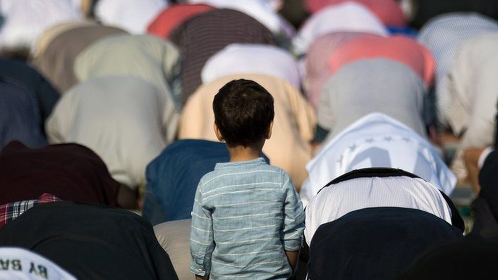 A young boy looks on as Muslims participate in a group prayer service during Eid al-Fitr, which marks the end of the Muslim holy month of Ramadan, in Bensonhurst Park in the Brooklyn, New York