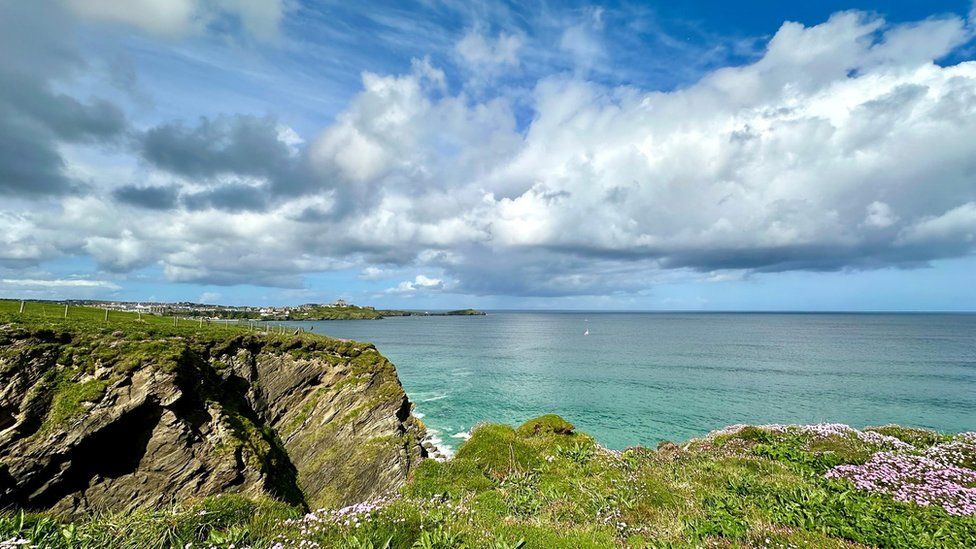 Cumulus clouds in a blue sky over a blue sea, with grass-topped cliffs in the foreground